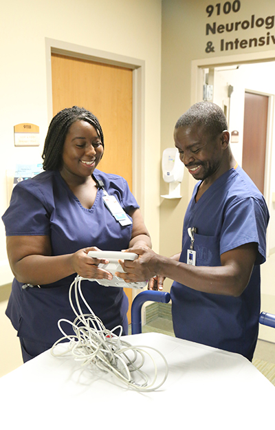 Unit 9100 nurse, Patricia Zatelia, RN, left, demonstrates a portable telemetry machine to visiting ICU nurse Felix Batson, RN. 